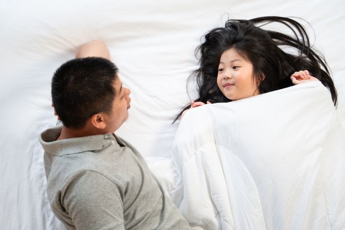 Asian father and daughter talking on bed.