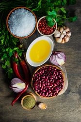 Top view of bowls of kidney beans, chili peppers, oil, garlic bulb and onions