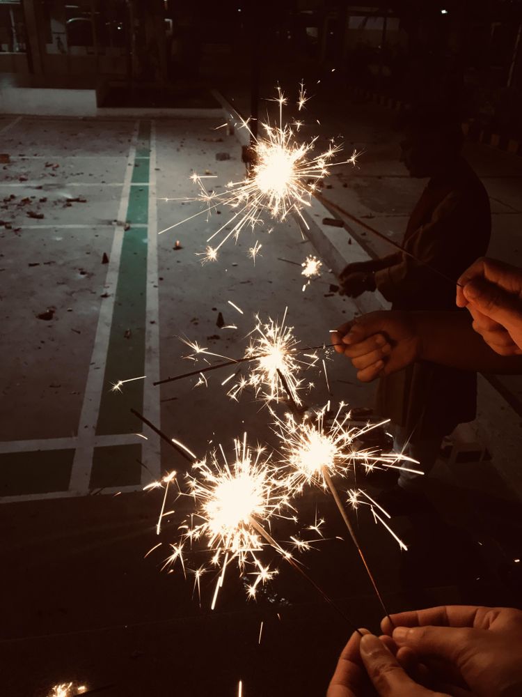 Cropped image of hands holding sparkling candles at night