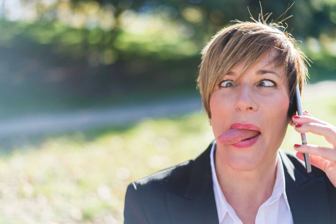 Businesswoman making silly face and talking on cellphone in park