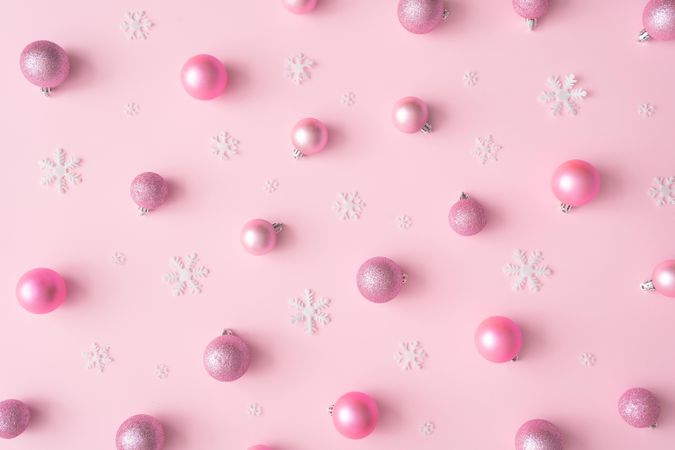 Different shades of pink baubles and snowflake decorations on a pink background
