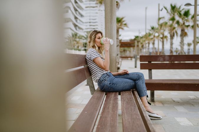 Happy woman with disposable cup of coffee sitting on street bench