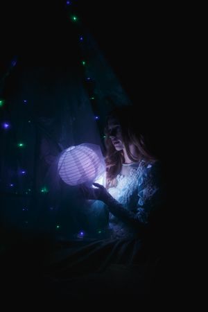 Portrait of woman in blue dress holding light paper lantern in a dark room