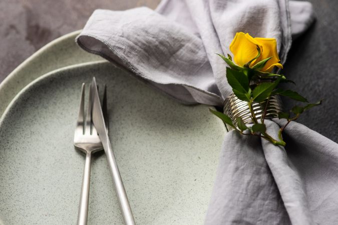 Grey table setting with single yellow rose and silverware