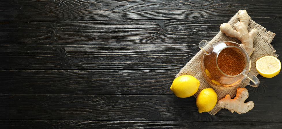 Teapot with tea, lemon and ginger on wooden background, space for text
