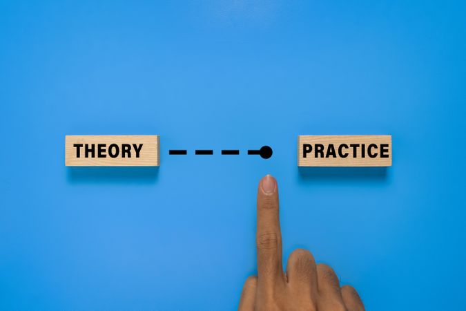 male hand point wooden blocks with theory and practice words. isolated on blue background. concept of implementing theory to practice