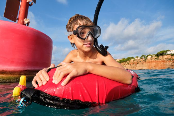 Happy kid in diving mask in seawater near red buoy