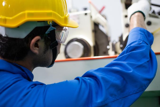 Male in blue jumpsuit and PPE gear operating controller in factory