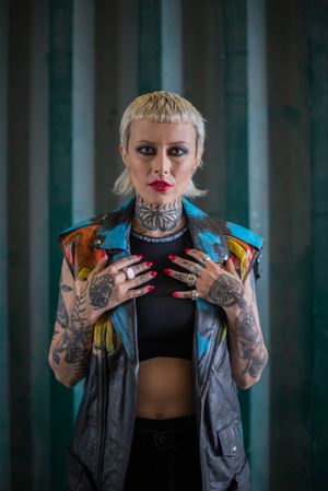 Young punk hipster woman with short blonde bangs poses in vest with full sleeve tattoos