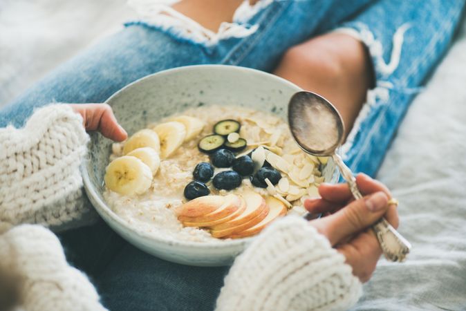 Close up of woman holding bowl of warm oatmeal with fruit, nuts, and honey