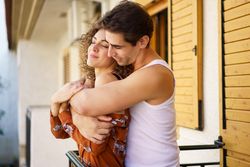 Loving couple engaged in romantic back hug on veranda of apartment