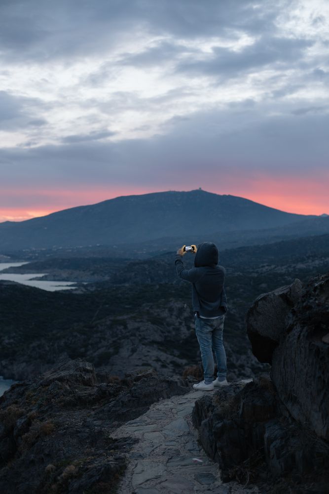 Male taking photo with smartphone on cliff at dusk