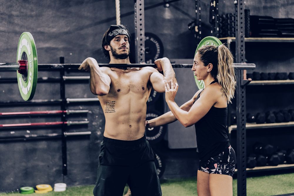 Muscular man lifting heavy weight in sport club and listening to personal trainer