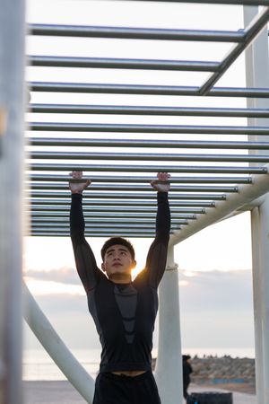 Asian sportsman exercising on monkey bars