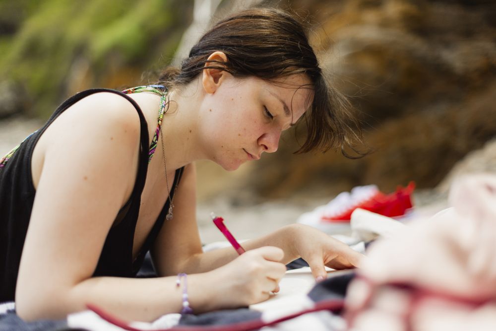 A young women writes her diary lying on the towel, while enjoying the outdoors