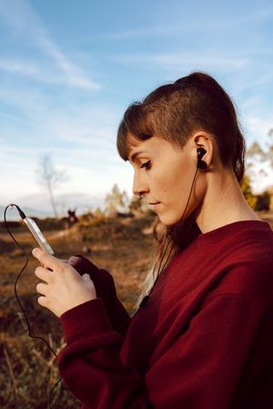Young woman with piercing listening music on smartphone on hill