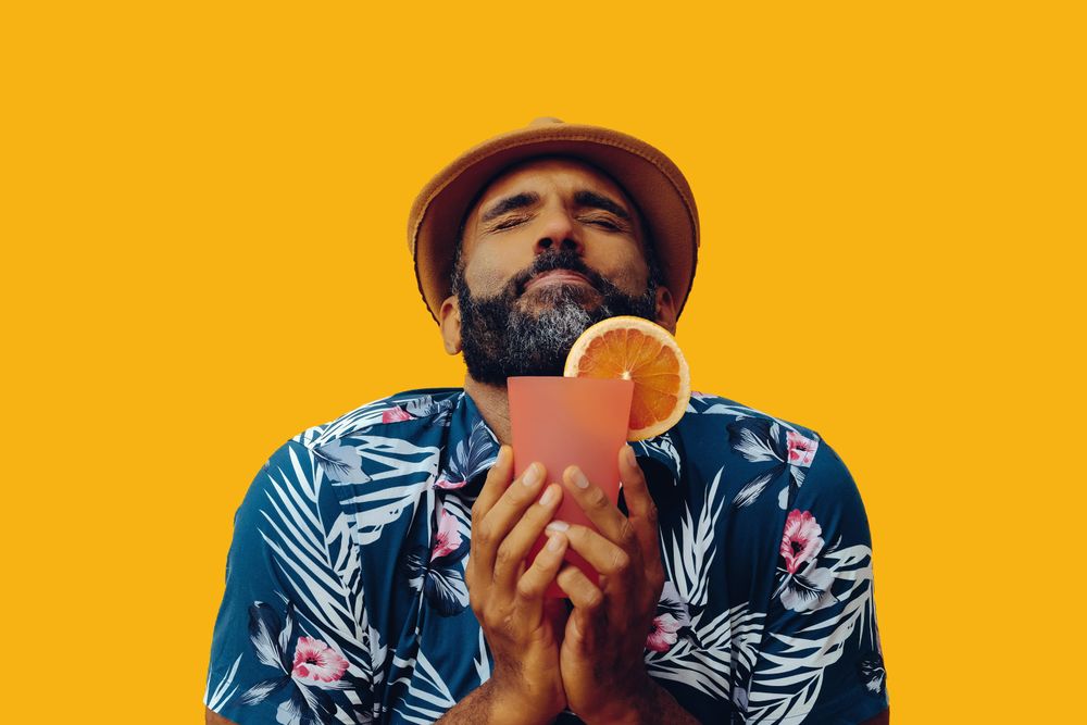 Male wearing colorful shirt and really enjoying a cocktail with yellow background