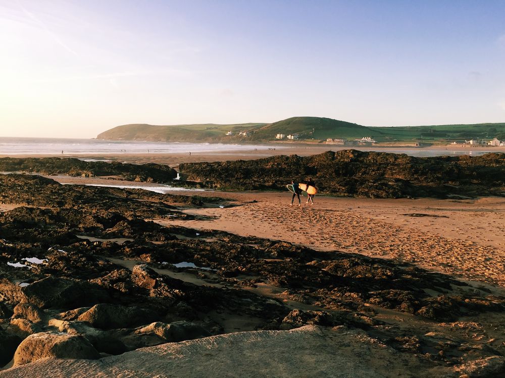 Surfers walking towards water at rugged coast line at dawn