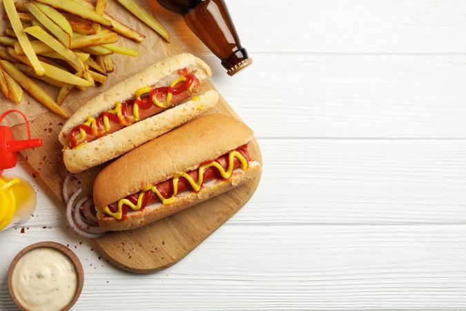 Tasty hot dogs, beer and sauces on plain wooden background