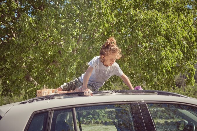 Attentive kid washing automobile roof in summer