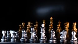 Silver and golden chess pieces on reflective board.