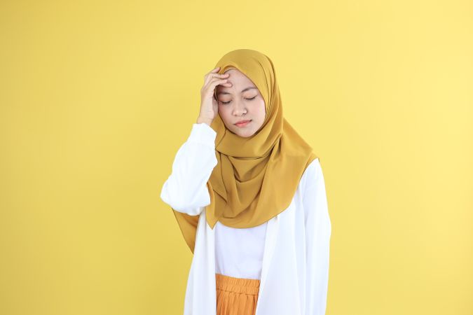 Stressed Asian Young Woman in White Shirt and Mustard Veil Touching his Head and Having Headache.