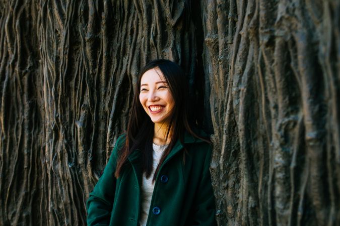 Cheerful Asian woman leaning on rough wall