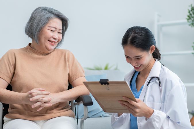 Mature Asian woman receiving medical care from doctor with clipboard