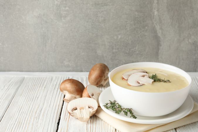 Close up of bowl of creamy mushroom soup with herbs on napkin on wooden table, copy space