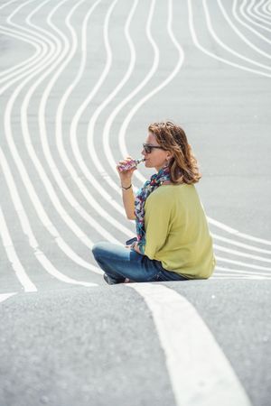 Modern relaxed woman vaping while sitting on marked road