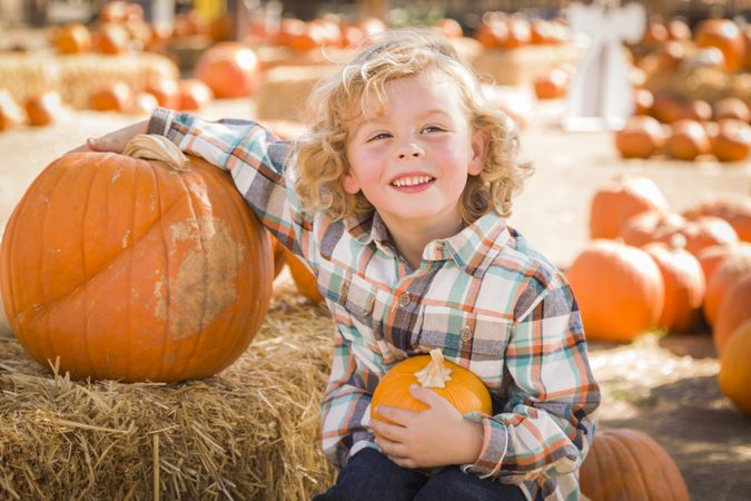 Little Boy Sitting and Holding His Pumpkin at Pumpkin Patch.