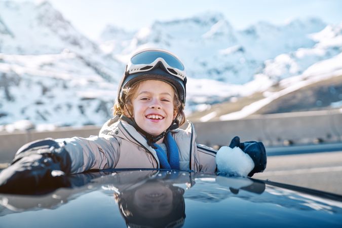 Joyful boy leaning on car roof with snowball