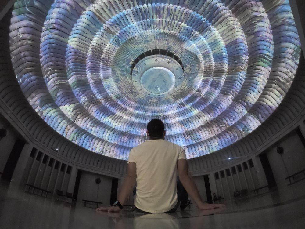 Back view of man in light shirt sitting in an spacious room looking at the round ceiling