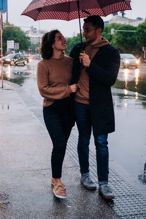 Happy couple with umbrella hugging on wet street