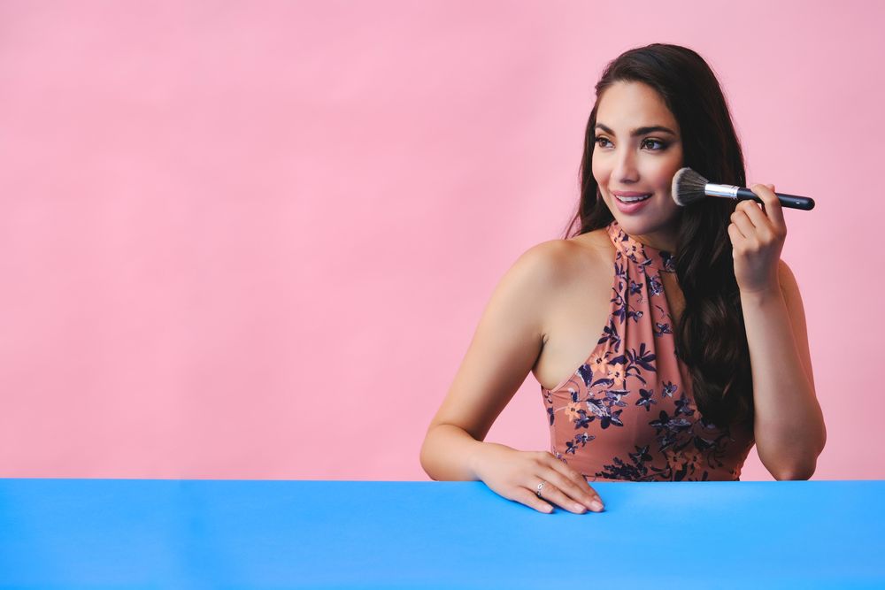 Happy smiling Hispanic woman with long brown hair holding large make up brush, copy space