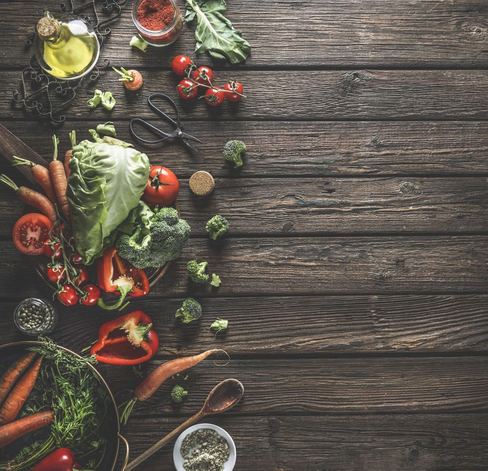 Food background with organic vegetables, healthy ingredients and kitchen utensils on dark rustic wooden table. Top view. Copy space.
