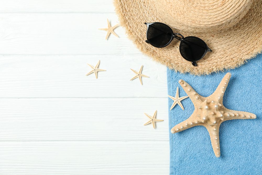 Straw hat, sunglasses, towel and starfishes on wooden background, space for text and top view. Summer vacation backdrop