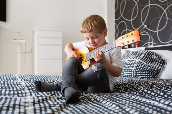Young blonde boy playing toy guitar