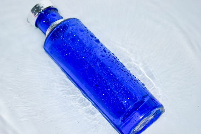 Blue perfume bottle on light background with water ripples
