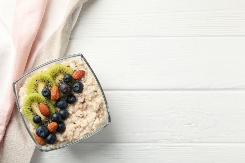 Towel and bowl with oatmeal porridge and fruits on wooden background