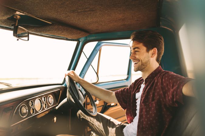Smiling male sitting in driver seat of old car