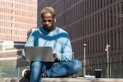 Stylish young Black man working remotely on laptop in city park