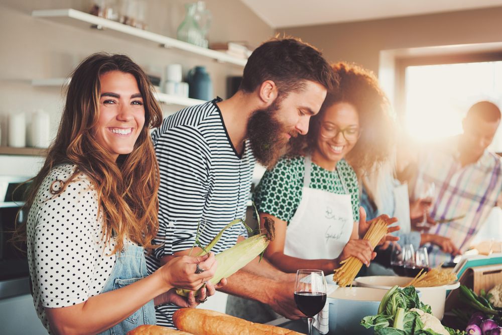 Smiling friends prepping salad and boiling pasta