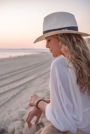 Charming woman in hat leaning on fence and looking at sea