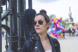 Front view of a young laughing hipster woman standing and leaning on a fence at park in sunny day while looking away