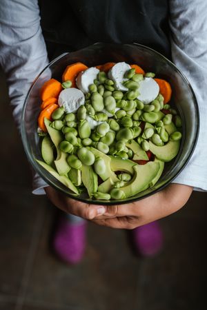 Hands of anonymous girl with vegetable salad in kitchen