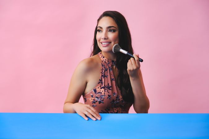 Happy woman with long brown hair holding large make up brush to her face, copy space