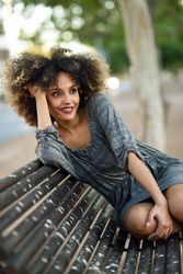 Happy female in casual dress sitting on park bench looking around, copy space