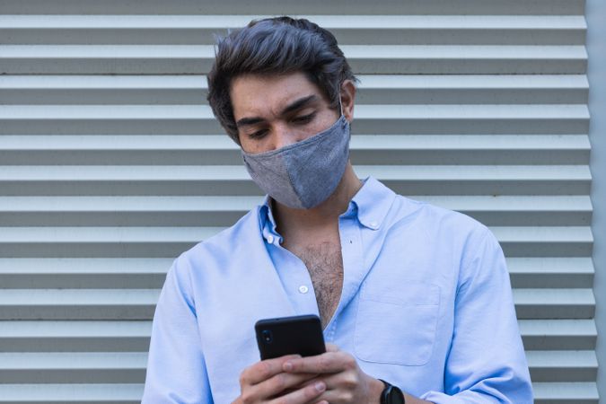 Man in mask browsing smartphone on street