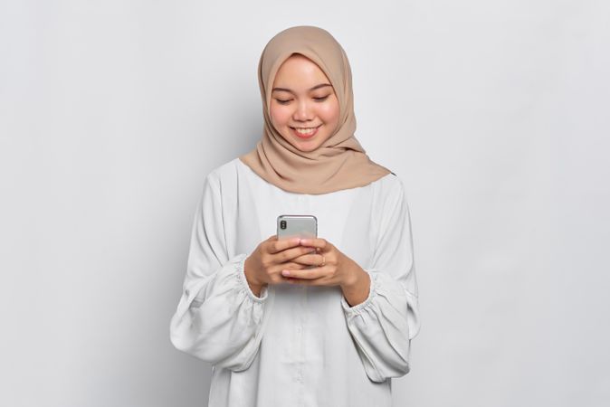 Happy Asian female in headscarf looking down at cell phone
